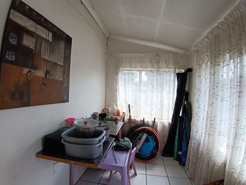 A utility space featuring tiled flooring and large windows, currently used for storage. The area shows signs of wear including wall and ceiling damage.