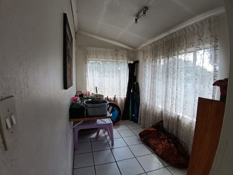 A utility or sunroom space featuring tiled flooring and large windows, currently used for storage. The area requires cosmetic updates to improve its condition.