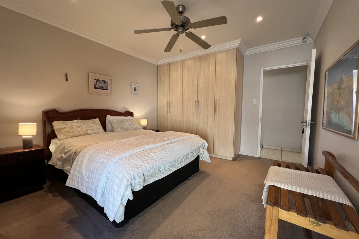 A well-maintained bedroom featuring built-in wooden cupboards, a ceiling fan, recessed lighting, and neutral carpeting.