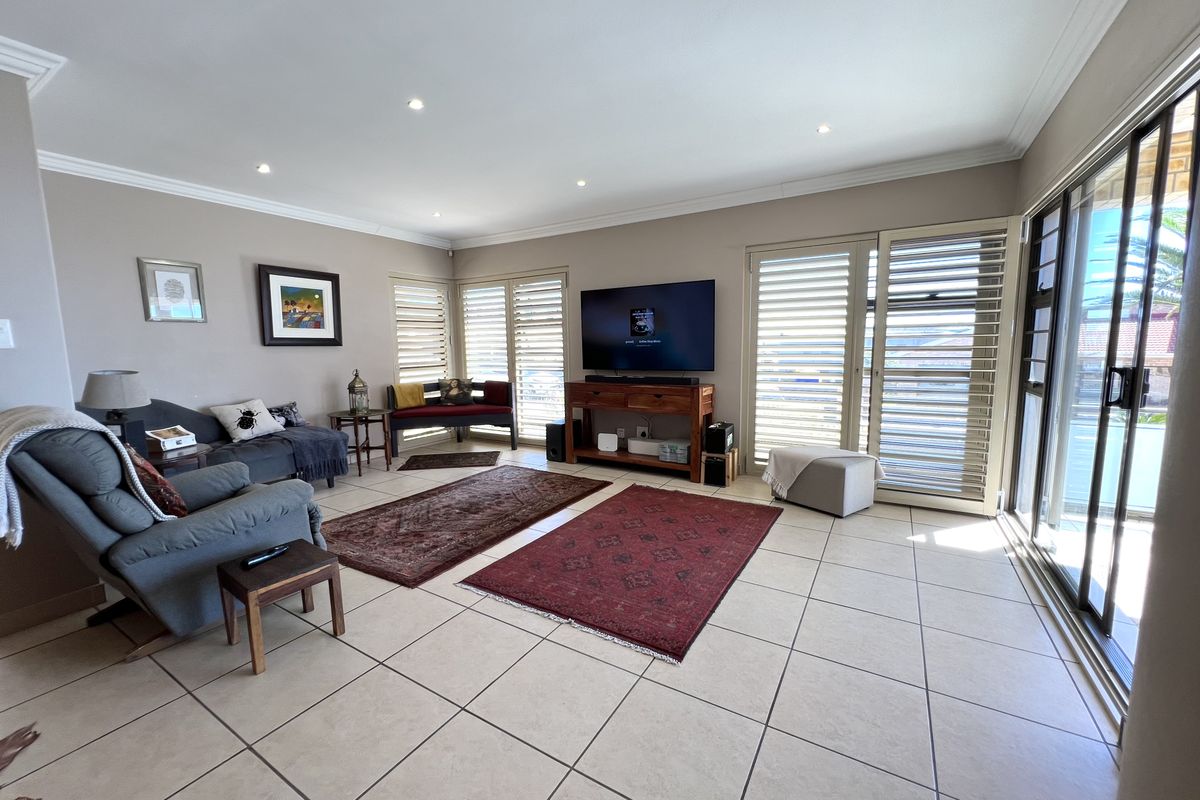Spacious living room featuring large format floor tiles, recessed downlighting, and sliding glass doors with integrated shutters providing access to the exterior.