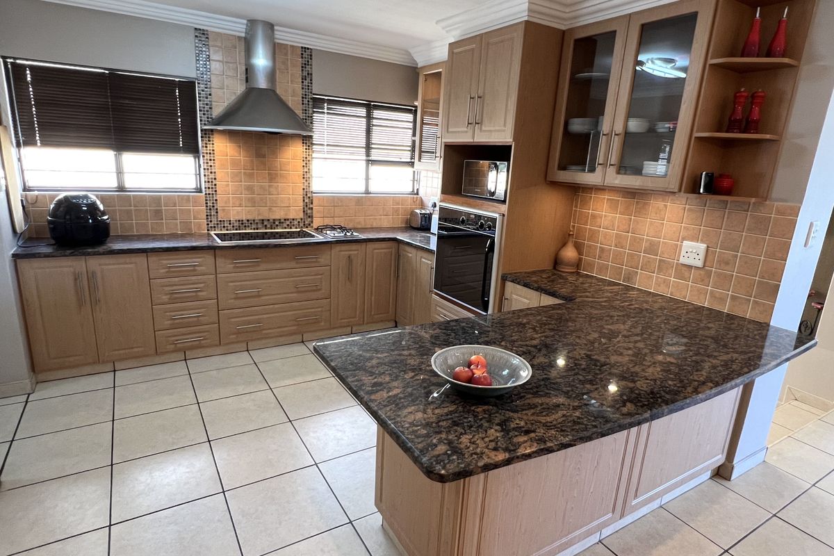 A functional kitchen featuring light wood cabinetry, dark granite countertops, tiled backsplash, built-in oven, extractor fan, and ceramic floor tiles.