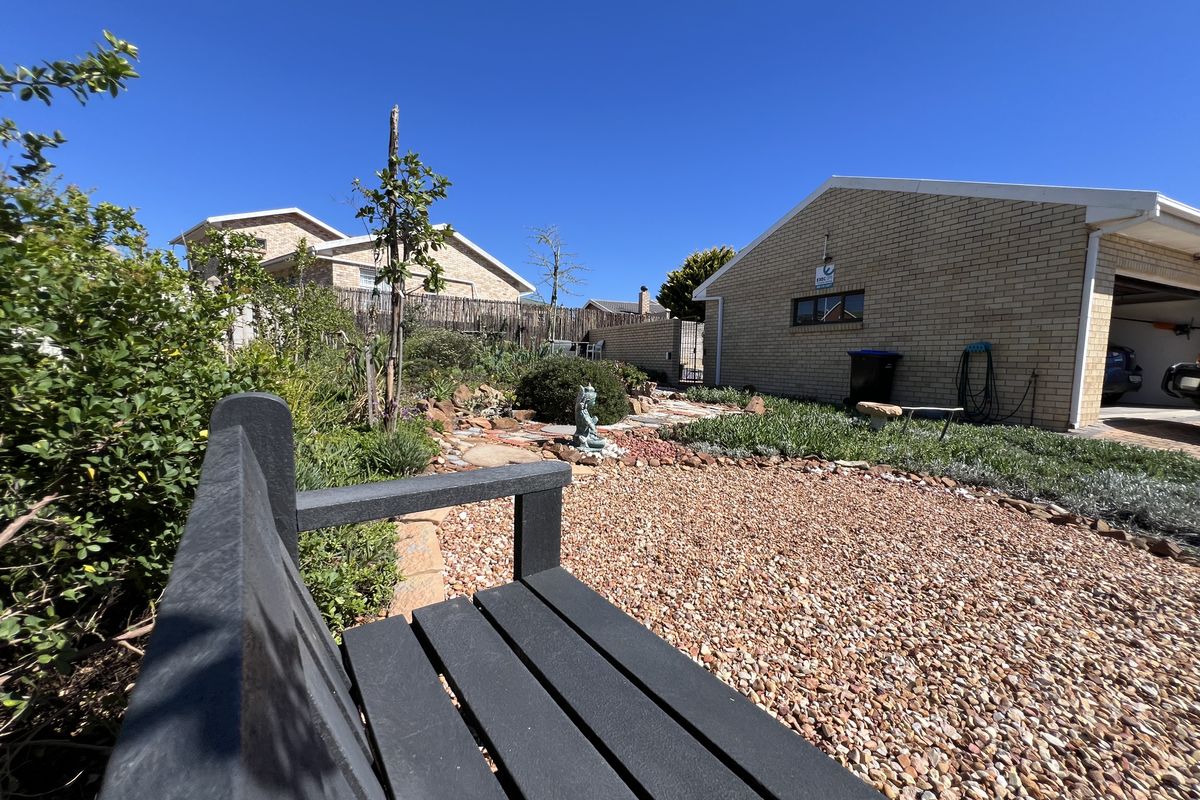 A well-maintained rear garden area featuring gravel landscaping, established shrubs, and a brick-built garage structure.