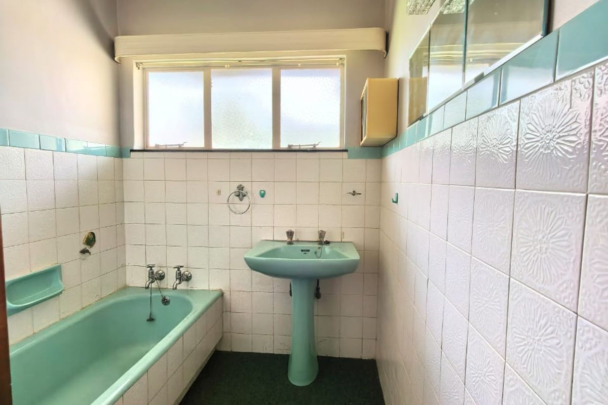 A dated bathroom featuring original pastel green sanitary ware, tiled walls, and a window, offering significant potential for a modern renovation.