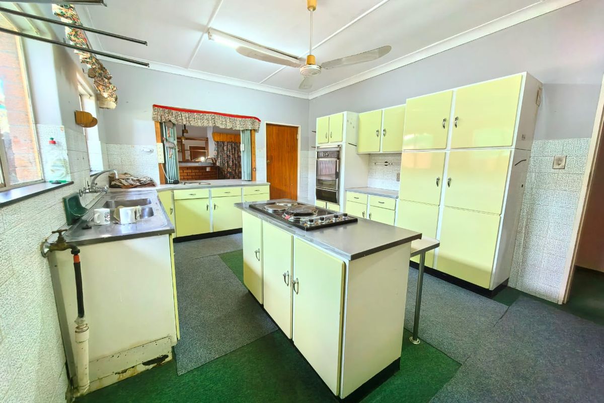 A dated kitchen featuring original cabinetry, a central island with a cooktop, built-in oven, and tiled splashbacks, offering significant potential for modernization.