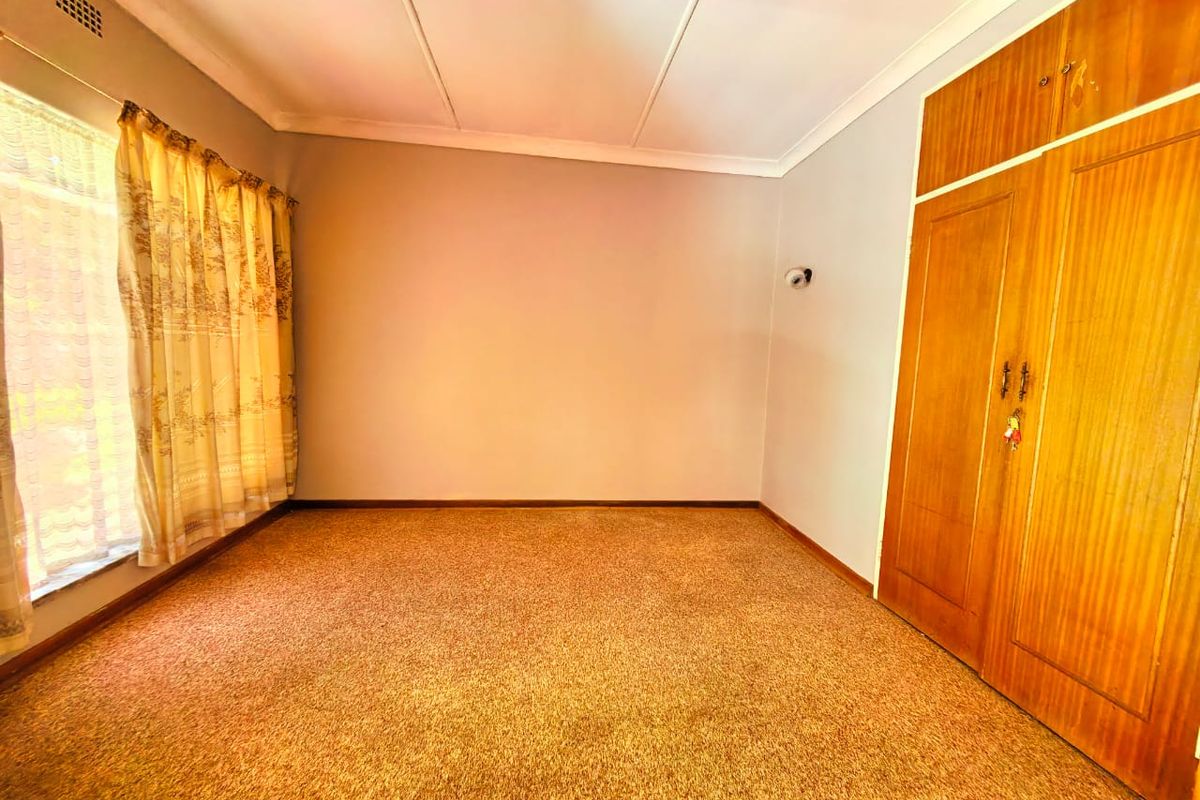 An empty bedroom featuring built-in wooden wardrobes, carpeted flooring, and a coved ceiling, offering a blank canvas for renovation.