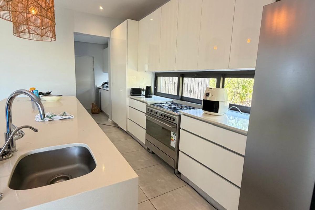 Modern kitchen featuring sleek white cabinetry, quartz countertops, a central island with a stainless steel sink, and a gas stove.