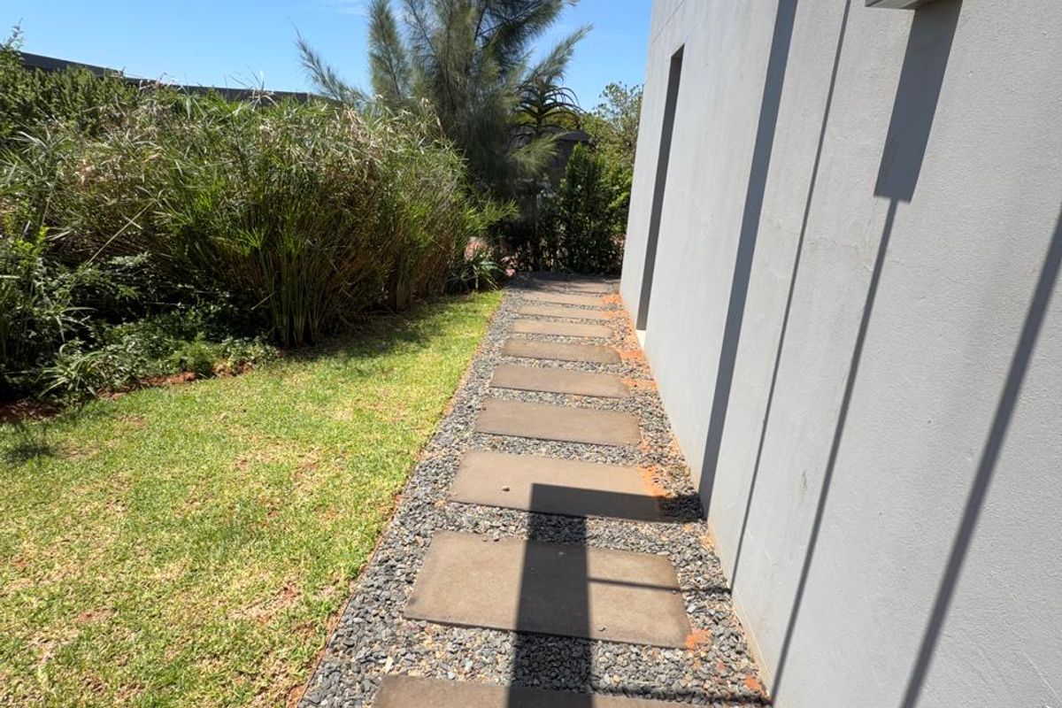 A clean exterior side path featuring stone pavers, gravel landscaping, and a modern pergola structure along the side of the building.