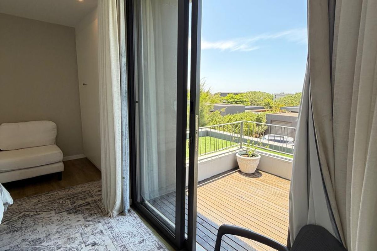 A bright bedroom featuring large sliding glass doors that open onto a private timber-decked balcony with a metal balustrade.