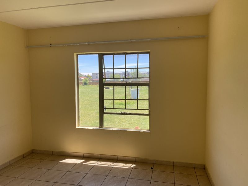 An empty bedroom featuring tiled flooring, a steel-framed window, and a curtain rail, offering a blank canvas for potential interior updates.