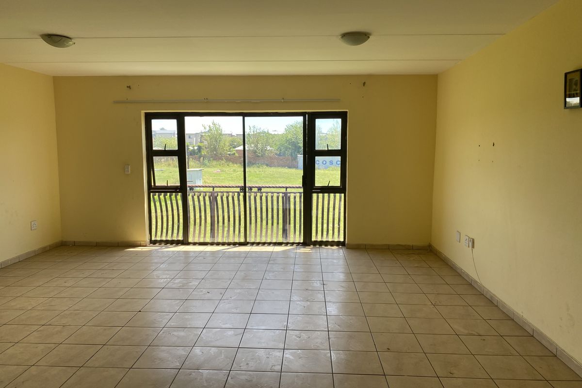 A spacious, empty living area featuring tiled flooring and a large sliding glass door that opens to an outdoor view.