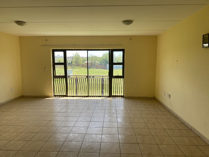 A spacious, empty living area featuring tiled flooring and a large sliding glass door that opens to an outdoor view.