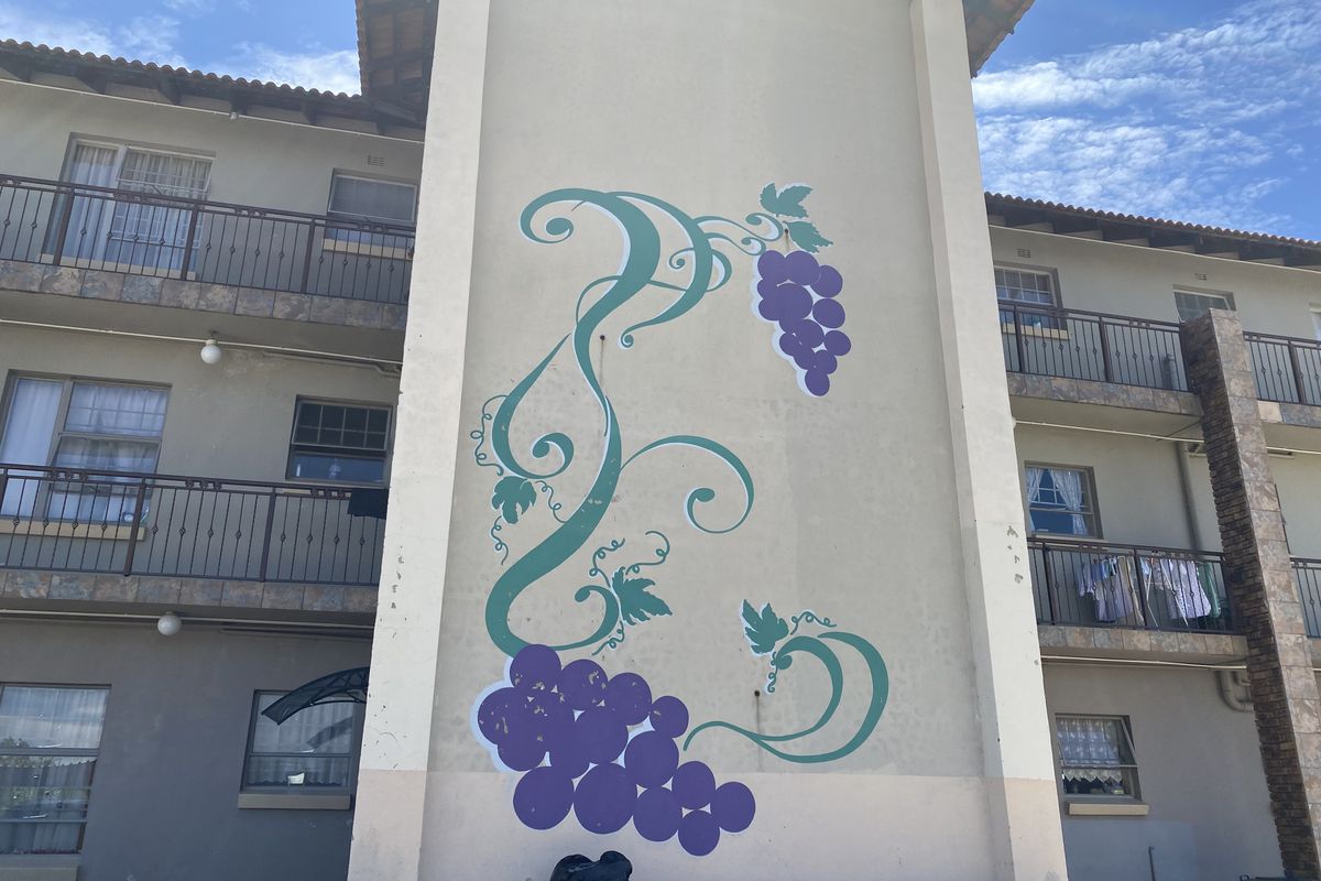 Exterior view of a townhouse complex featuring a decorative grape mural on the central pillar and wrought iron balcony railings.
