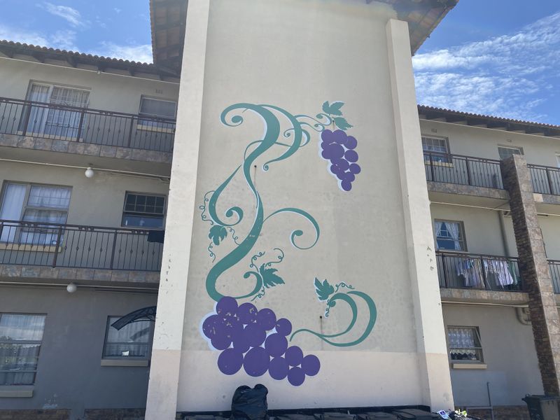 Exterior view of a townhouse complex featuring a decorative grape mural on the central pillar and wrought iron balcony railings.