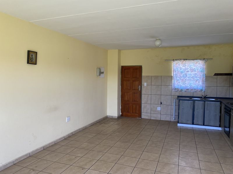 An open-plan living and kitchen area featuring tiled flooring, built-in cabinetry, and a functional kitchen layout, ready for cosmetic updates.