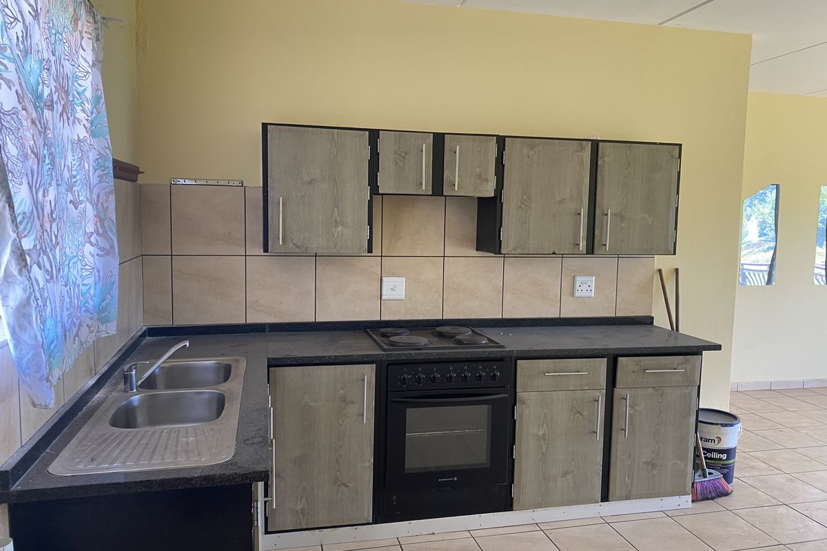 A functional kitchen featuring wood-look cabinetry, dark laminate countertops, a built-in oven and hob, and tiled backsplash with neutral floor tiles.