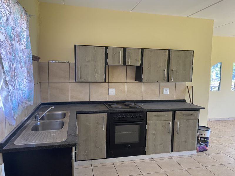 A functional kitchen featuring wood-look cabinetry, dark laminate countertops, a built-in oven and hob, and tiled backsplash with neutral floor tiles.