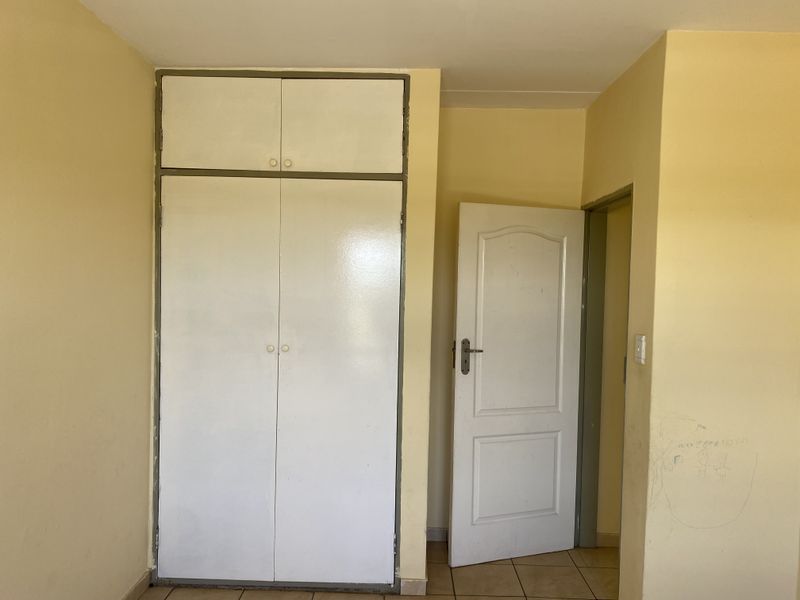 An empty bedroom featuring built-in wardrobes, tiled flooring, and a standard internal door, requiring minor cosmetic updates to the wall finishes.