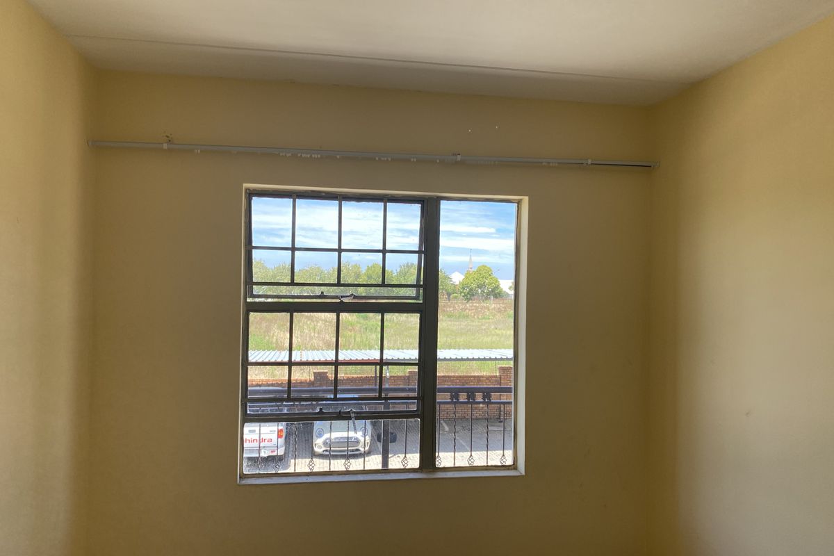 An empty bedroom featuring tiled flooring, a steel-framed window with a curtain rail, and neutral wall finishes.