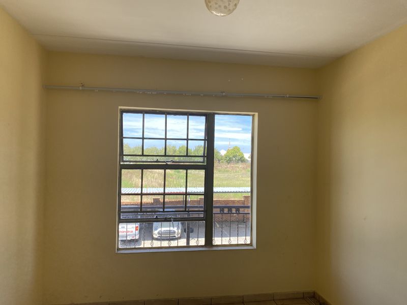 An empty bedroom featuring tiled flooring, a steel-framed window with a curtain rail, and neutral wall finishes.