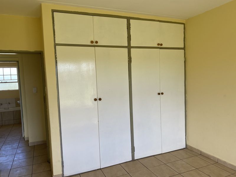 A bedroom featuring built-in cupboards with tiled flooring, showing signs of wear and dated finishes, offering potential for modernization.