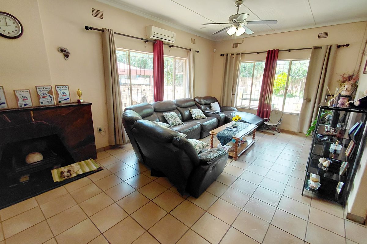 A spacious living room featuring tiled flooring, a built-in fireplace, and a ceiling fan, with large windows providing natural light.