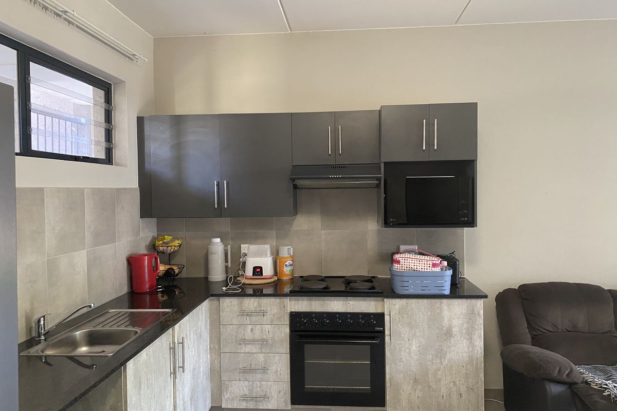 A compact kitchen featuring dark grey upper cabinetry, light textured lower cabinets, granite countertops, a built-in oven, and a stainless steel sink.