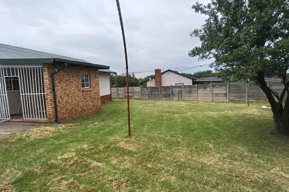 A spacious rear garden featuring a brick exterior wall, security bars on the entrance, and a precast concrete perimeter fence.