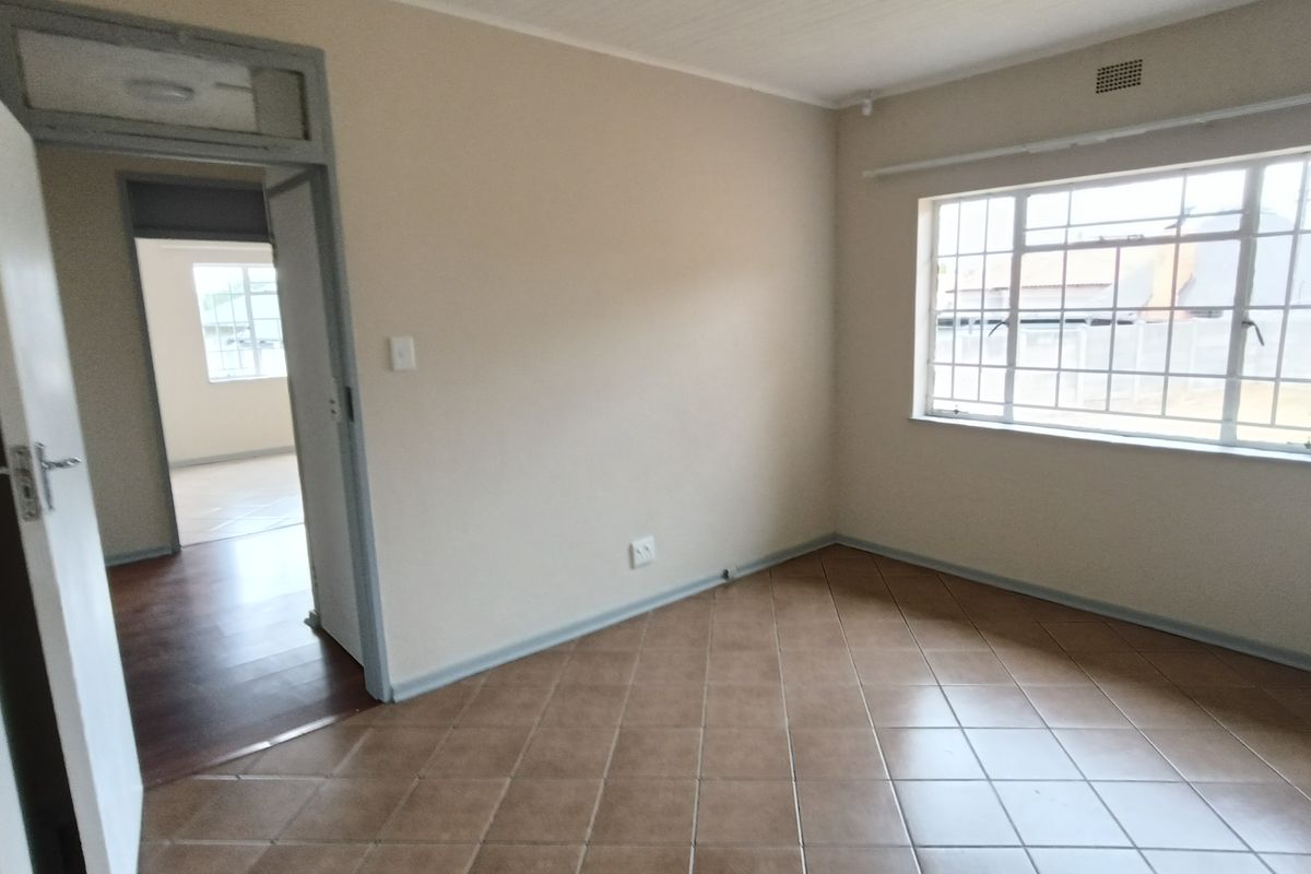 An empty bedroom featuring tiled flooring, a large window with security bars, and a doorway leading to an adjacent room.