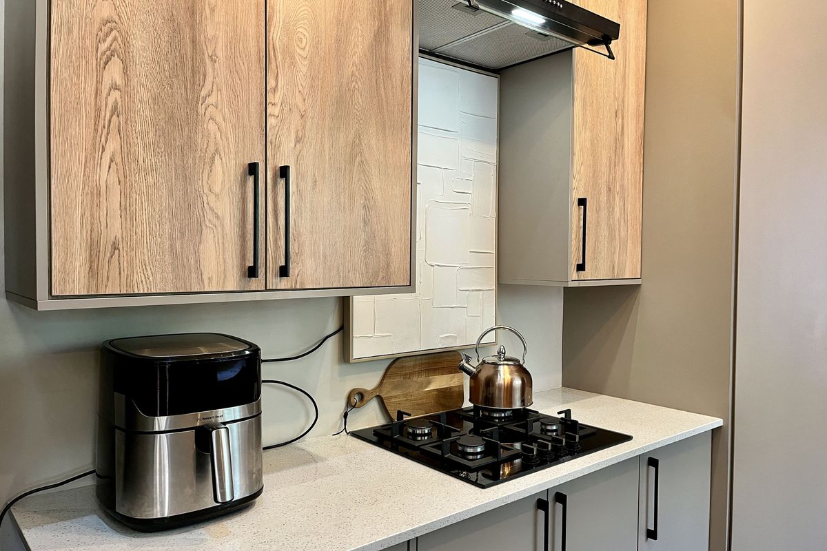 Modern kitchen featuring light wood-grain cabinetry, stone countertops, a built-in gas hob, and a sleek extractor fan.