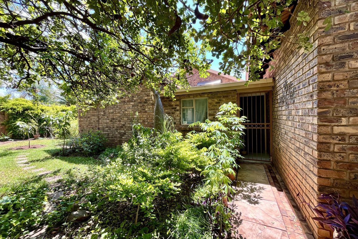 A view of the side entrance featuring a brick facade, paved walkway, and established garden surroundings under a mature tree canopy.