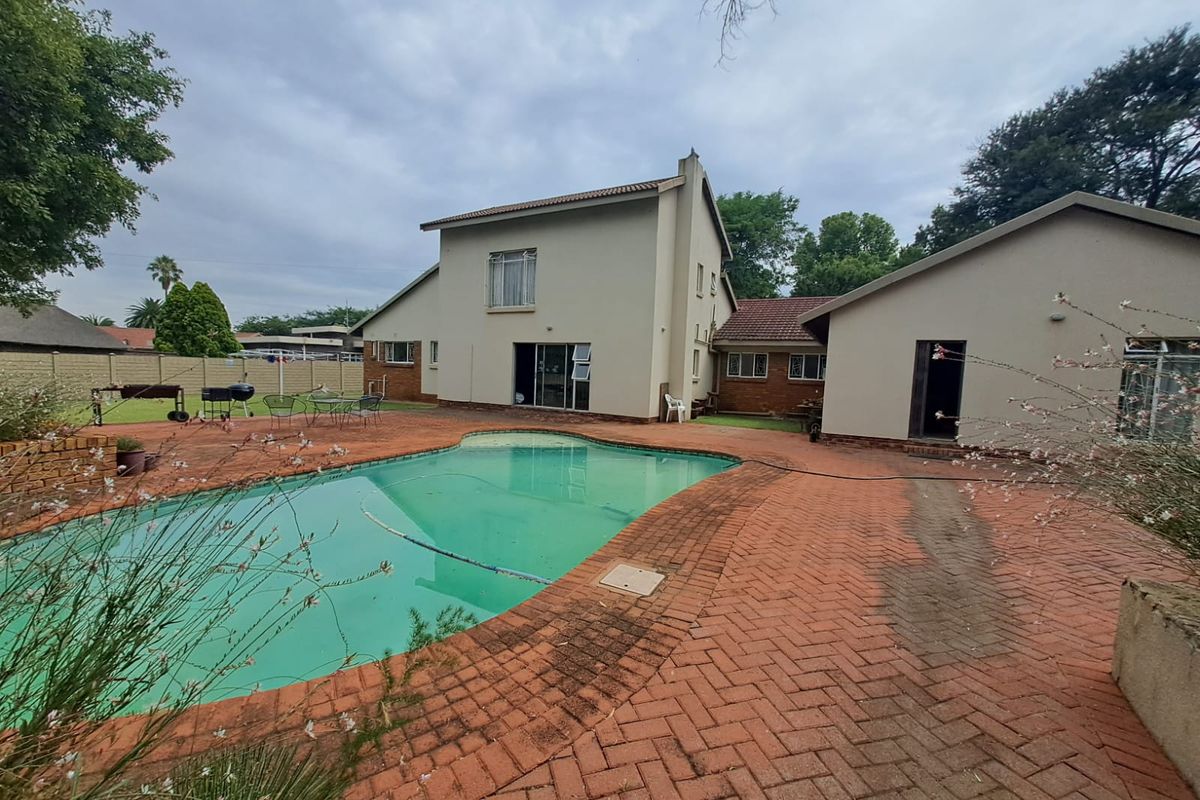 Rear view of the property featuring a swimming pool, extensive brick paved patio area, and a multi-level residential structure with a garden.