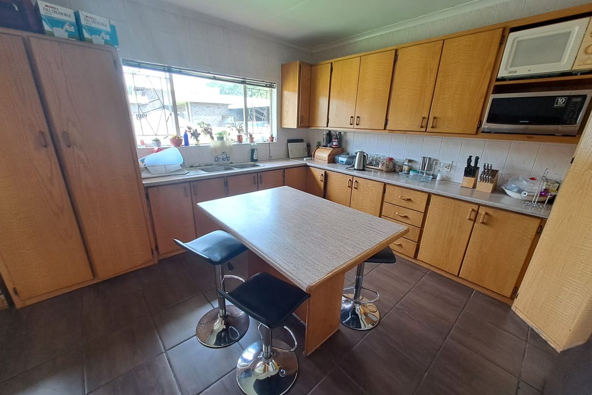 A functional kitchen featuring extensive wooden cabinetry, tiled flooring, a central breakfast island, and a double sink with a window view.