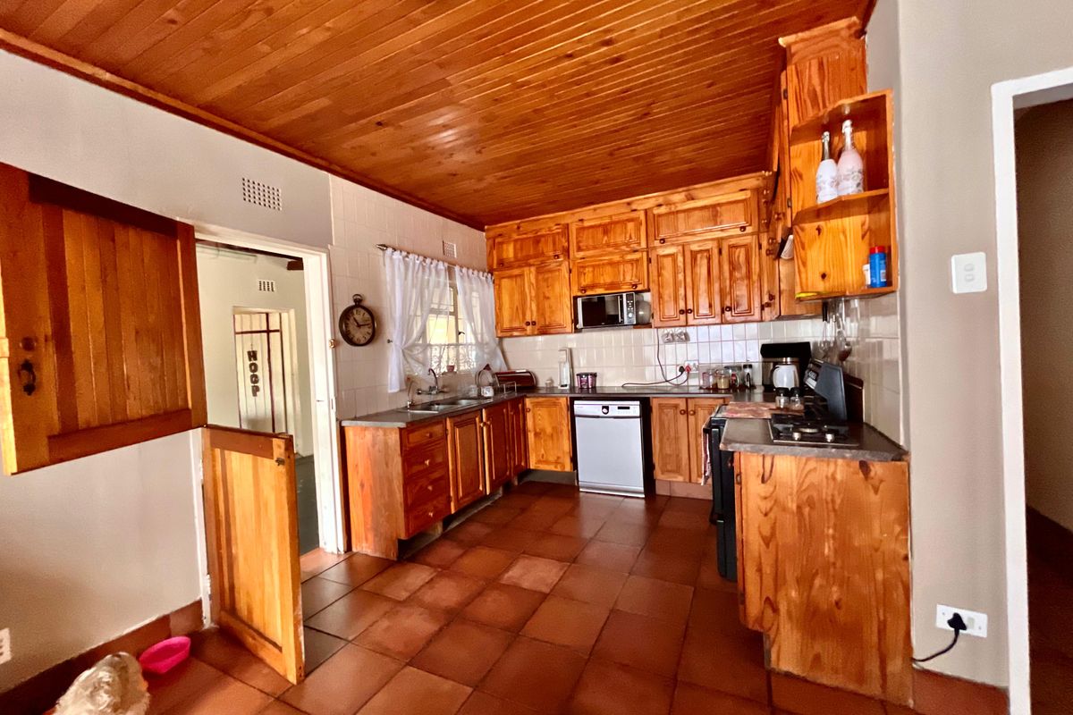 A traditional kitchen featuring extensive timber cabinetry, a wooden ceiling, tiled flooring, and a built-in stove and oven setup.
