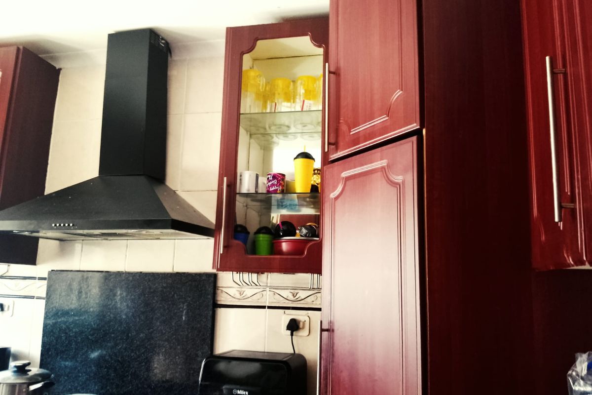 A kitchen area featuring dark red cabinetry, a black extractor fan, and a tiled backsplash with a decorative border.