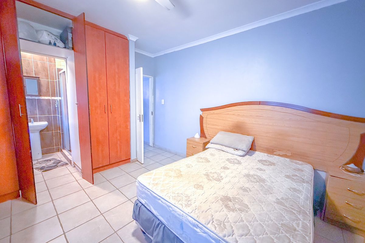Bedroom featuring built-in wooden cupboards, tiled flooring, and an en-suite bathroom with a pedestal basin and shower.