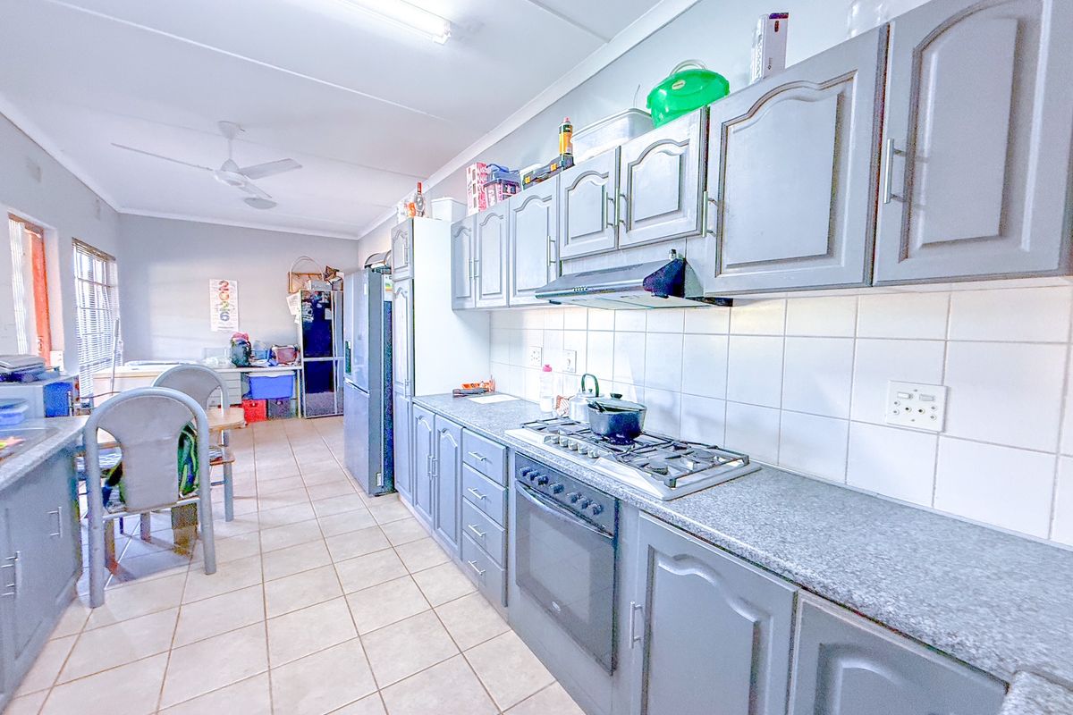 A functional kitchen featuring grey cabinetry, a built-in gas hob, an extractor fan, and tiled flooring, flowing into an adjacent dining area.