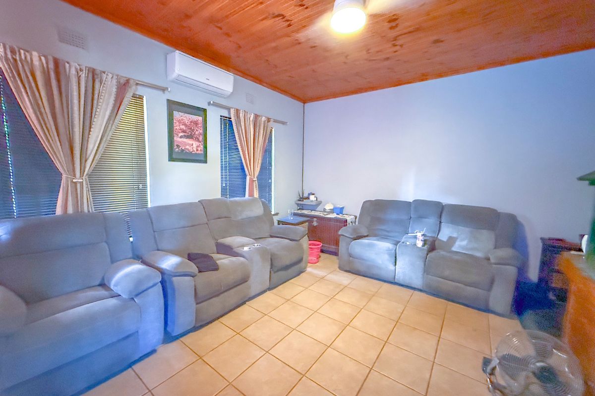 A living room featuring a timber-paneled ceiling, tiled flooring, and a wall-mounted air conditioning unit.