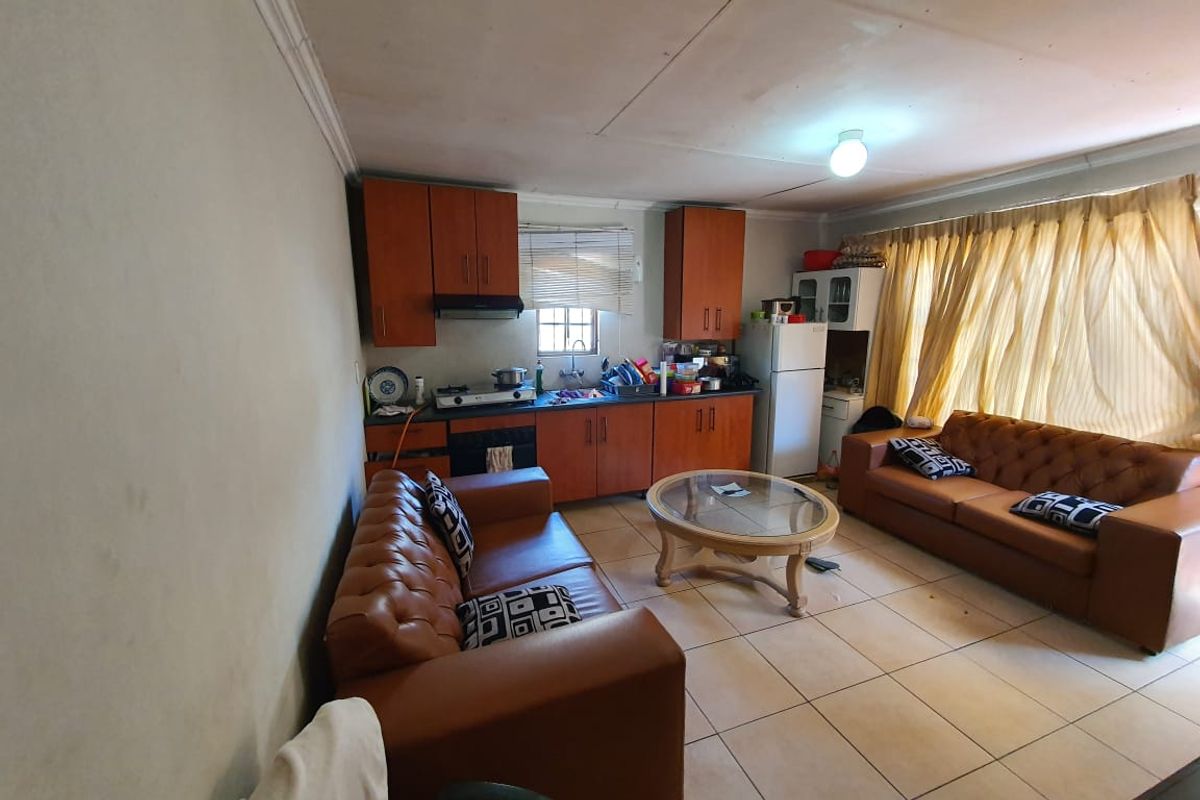 Open-plan living area featuring a compact kitchen with built-in cabinetry, cooktop, and tiled flooring throughout.