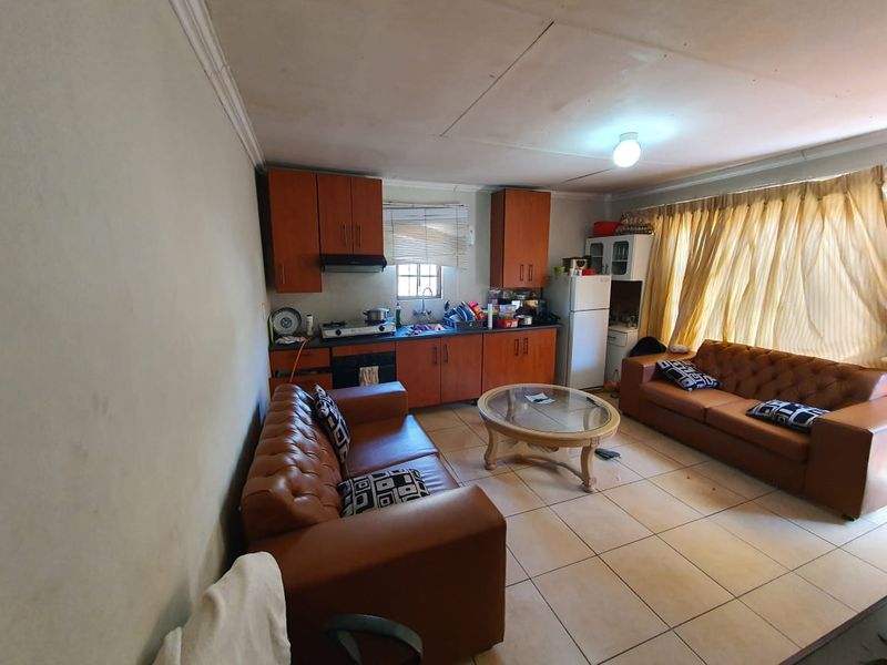 Open-plan living area featuring a compact kitchen with built-in cabinetry, cooktop, and tiled flooring throughout.