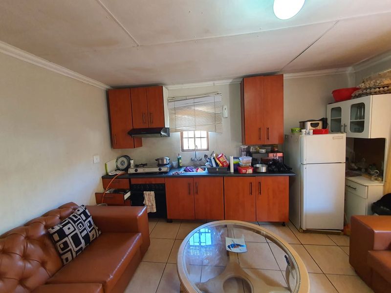 Open plan kitchen area featuring wooden cabinetry, built-in oven and hob, and tiled flooring, requiring cosmetic updates to improve the overall aesthetic.