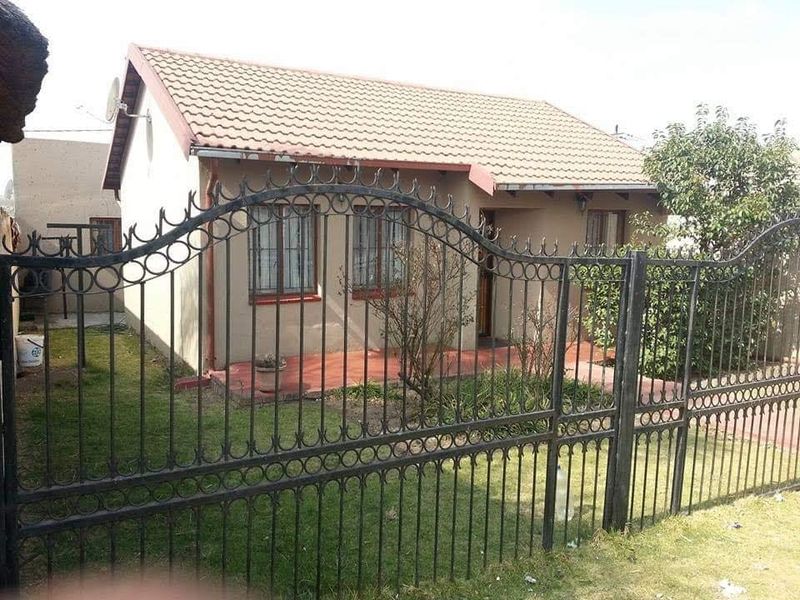 Front view of a single-story house featuring a tiled roof, security-barred windows, and a secure wrought iron perimeter fence with a front garden.