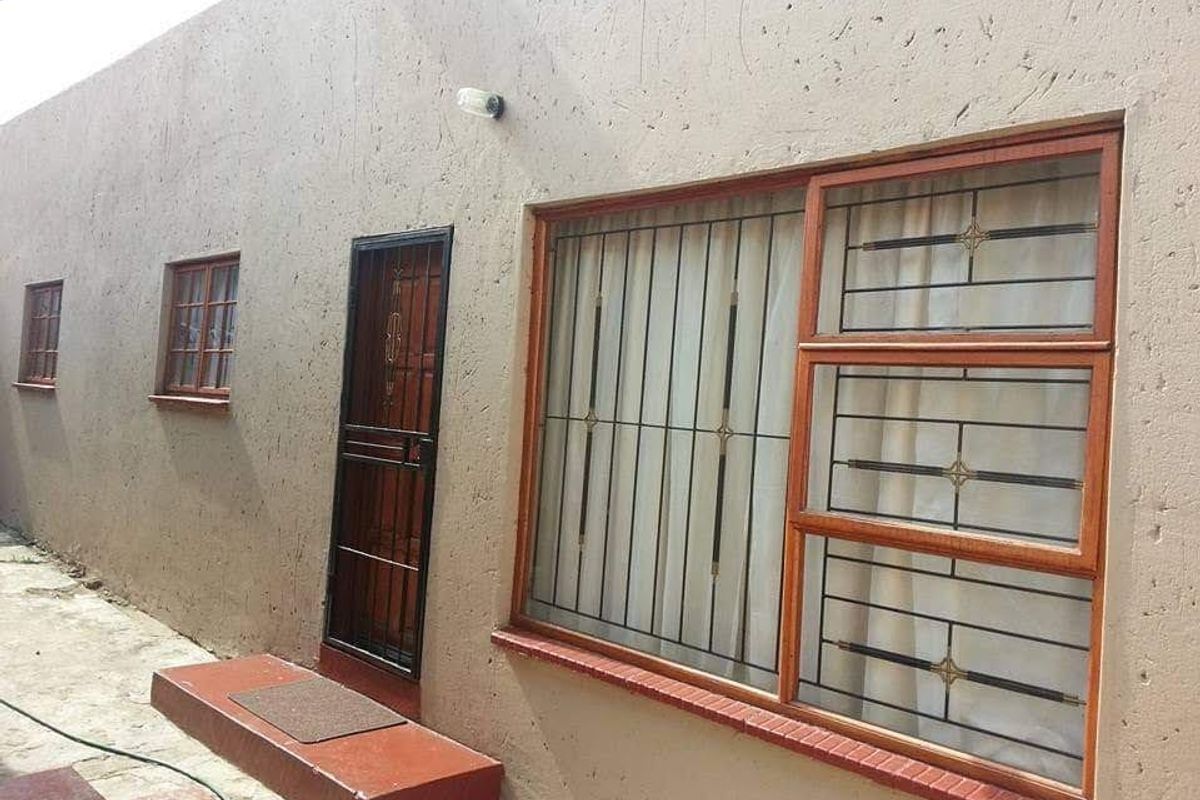 Rear exterior view of the property featuring plastered walls, wooden window frames with security bars, and a metal security gate.