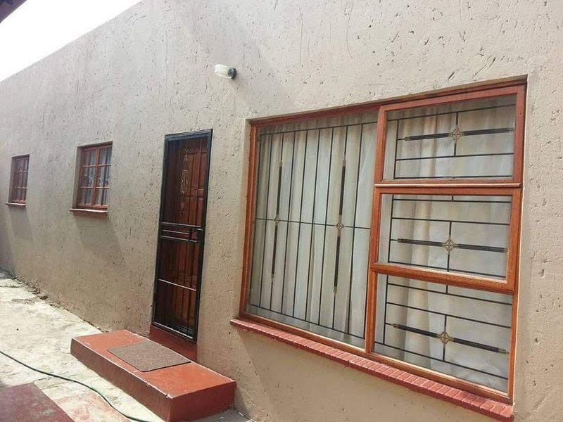 Rear exterior view of the property featuring plastered walls, wooden window frames with security bars, and a metal security gate.