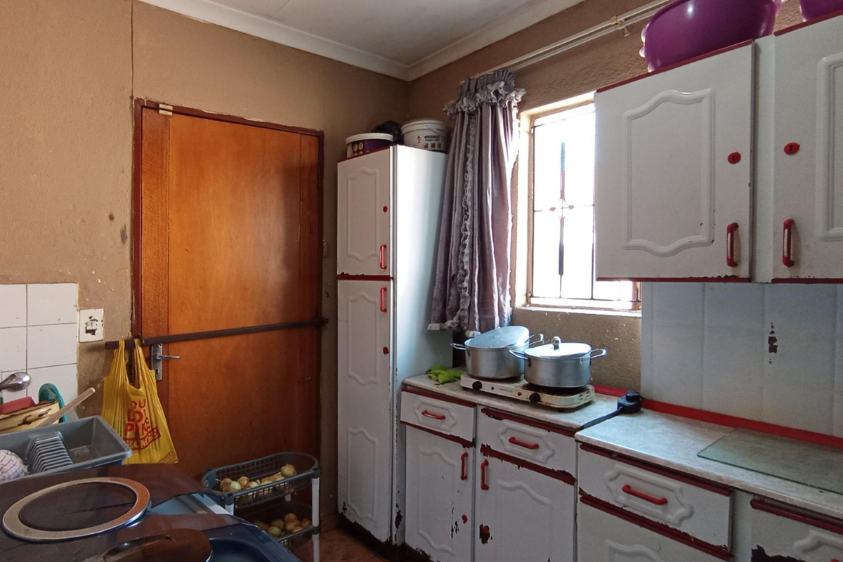 A functional kitchen featuring built-in cabinetry, a sink, and tiled splashbacks. The space shows signs of wear and would benefit from cosmetic updates.