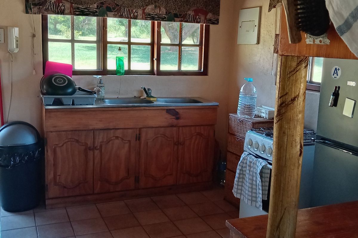 A rustic kitchen area featuring wooden cabinetry, a stainless steel sink, and a freestanding gas stove with tiled flooring.