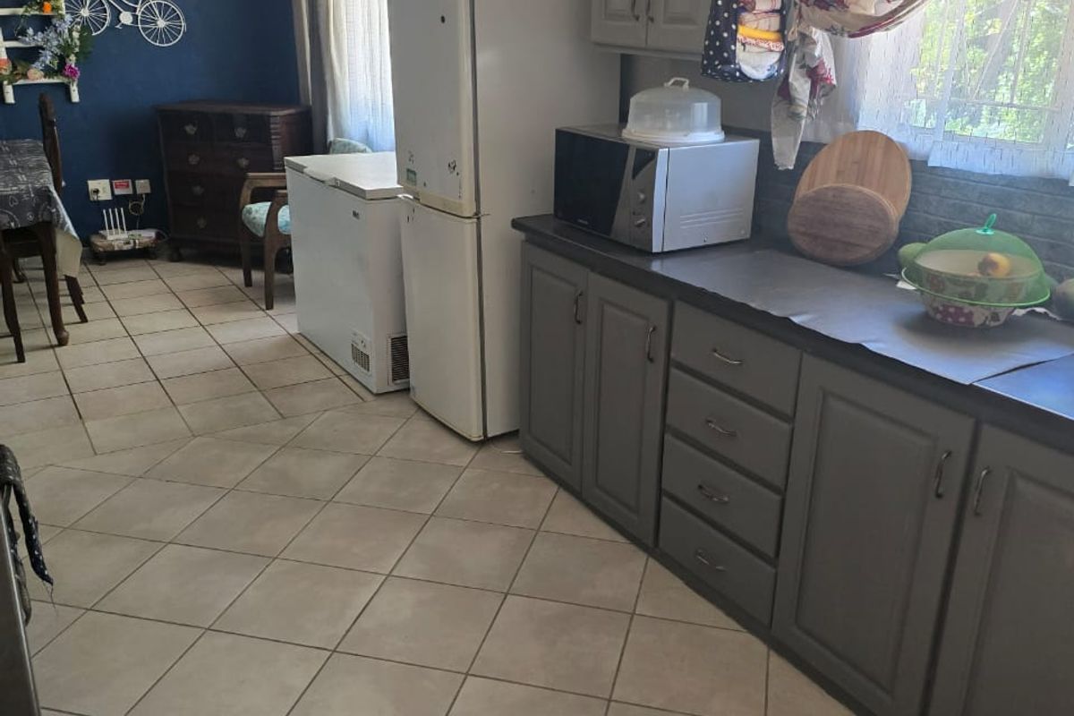 A functional kitchen area featuring grey cabinetry, tiled flooring, and an open-plan layout connecting to the dining space.