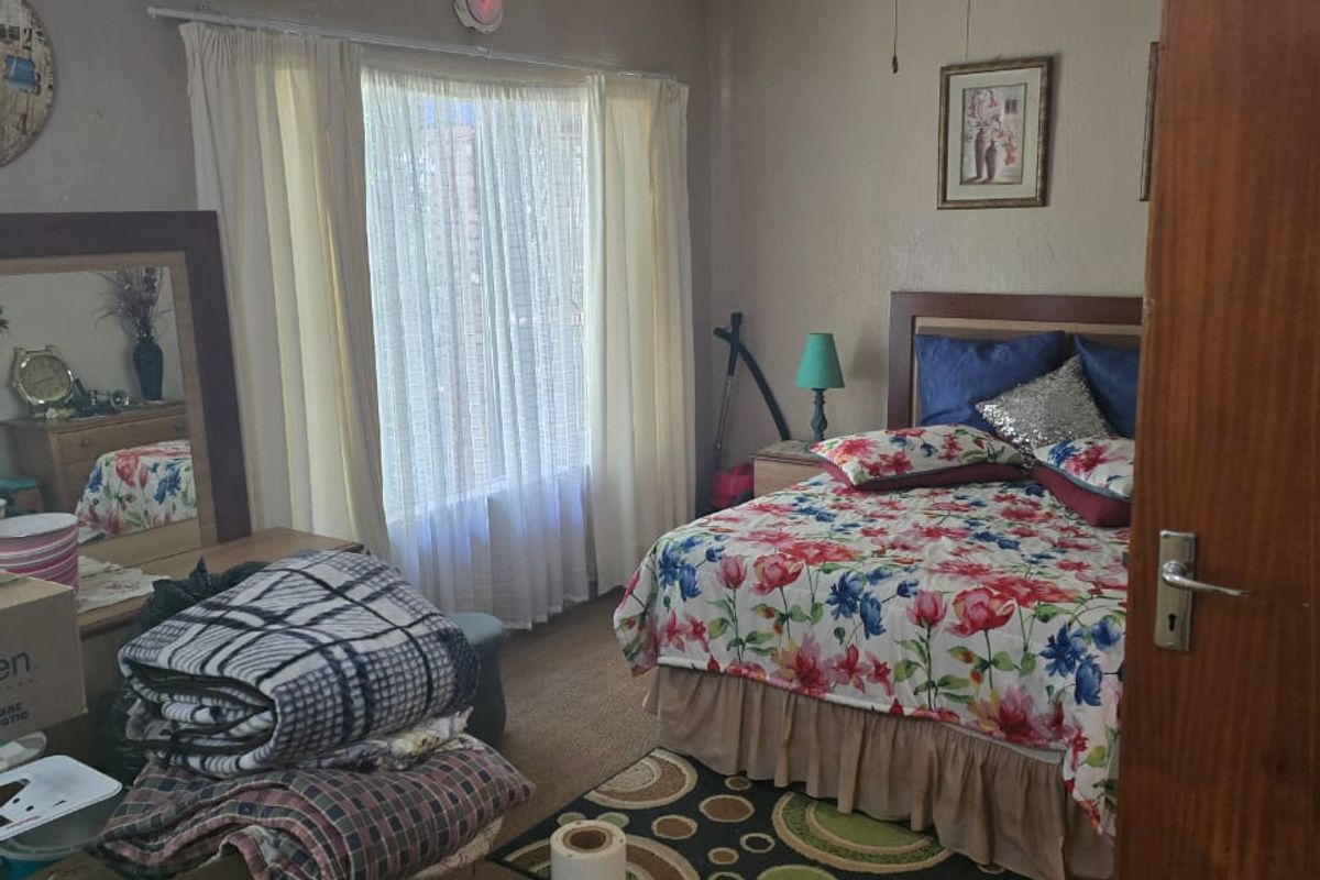 A bedroom featuring a ceiling fan, carpeted flooring, and a large window with curtains, offering a functional space for rest.