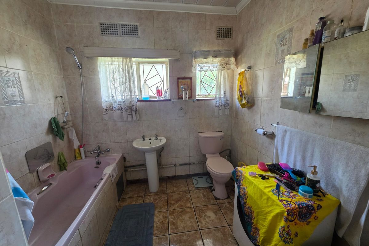 A dated bathroom featuring a pink bathtub, pedestal basin, and toilet with full-height wall tiling and tiled flooring.