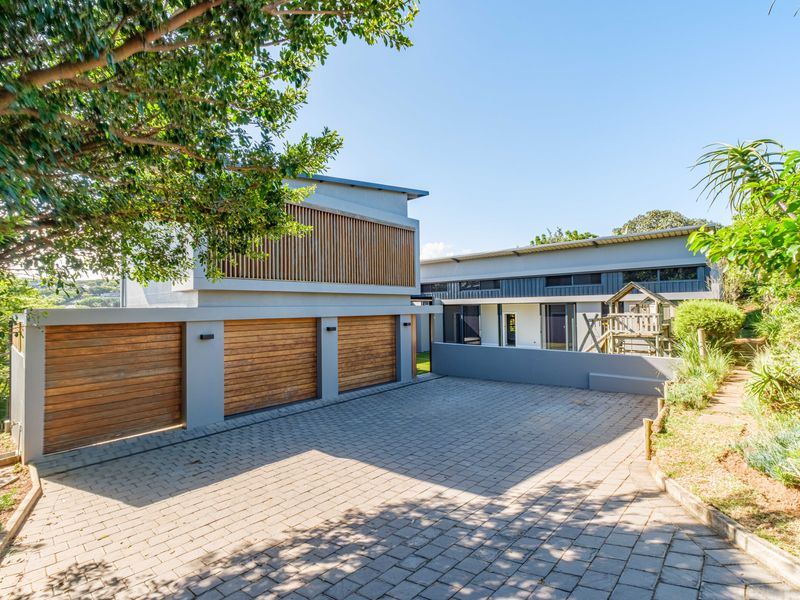 Modern architectural home exterior featuring a triple garage with timber doors, paved driveway, and clean contemporary lines.