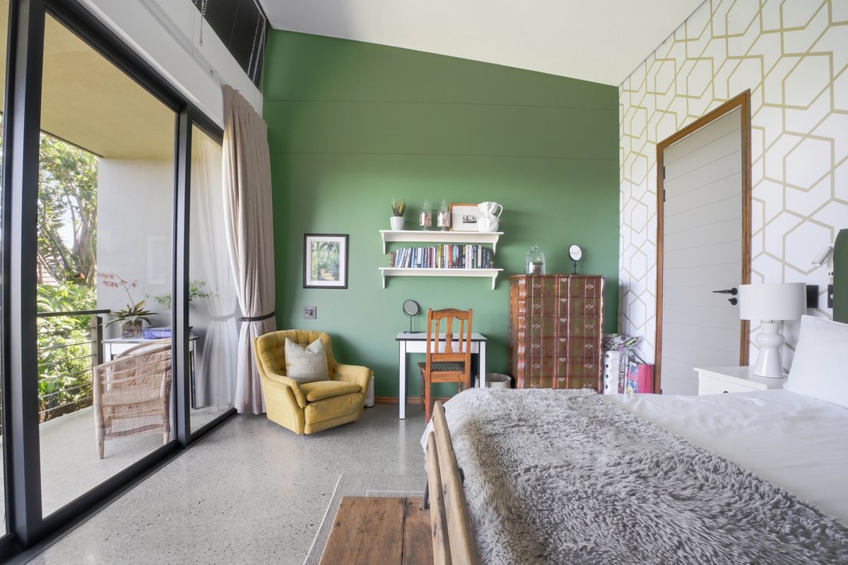 A bright bedroom featuring polished concrete floors, a high raked ceiling, and large sliding glass doors opening onto a private balcony.